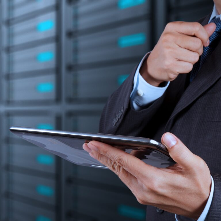 A person in a business suit holds a tablet and adjusts their tie while standing in front of rows of server racks, showcasing the efficiency of goods-to-person technology in a modern data center.