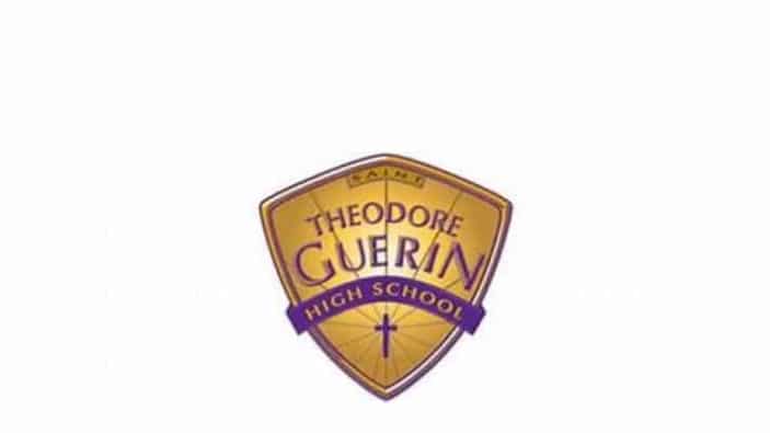 A gold and purple shield-shaped logo for Theodore Guerin High School with the word Saints at the top and a small cross at the bottom.