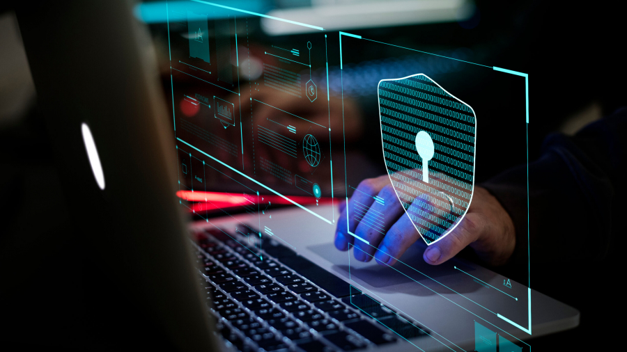 A person uses a laptop with a digital graphic of a security shield and keyhole overlayed on the screen, symbolizing cybersecurity and data protection.