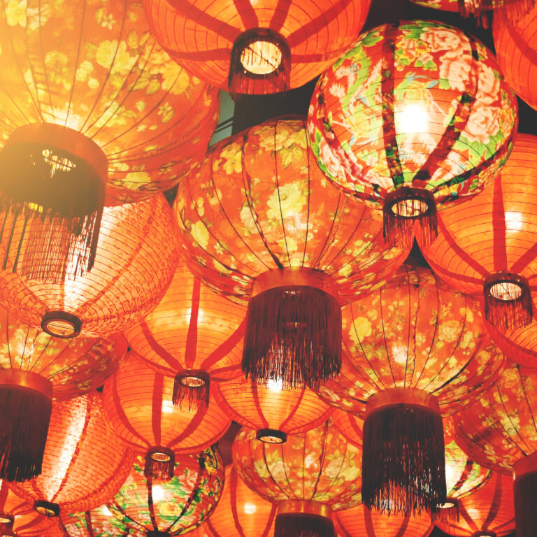 A cluster of traditional red paper lanterns with floral patterns and tassels, hanging closely together and glowing warmly, creating a festive and vibrant atmosphere.