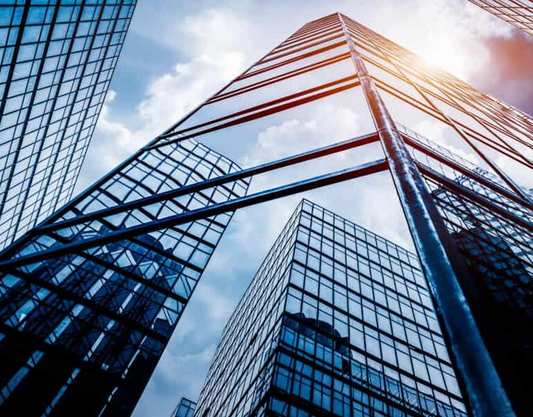 Tall glass skyscrapers reflecting the sky and clouds, viewed from below, with sunlight shining between the buildings, creating a modern and urban cityscape.