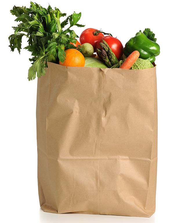 A brown paper grocery bag filled with fresh produce—celery, tomatoes, an orange, lettuce, asparagus, green bell pepper, carrot, and cabbage—sits against a white background, symbolizing the efficiency of transportation network optimization in delivery.