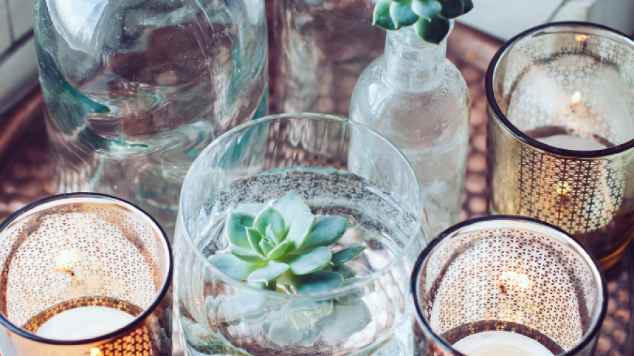 A decorative tray displays glass bottles with succulents inside, a glass bowl with a floating succulent, and three lit candle holders, creating a cozy and elegant arrangement.