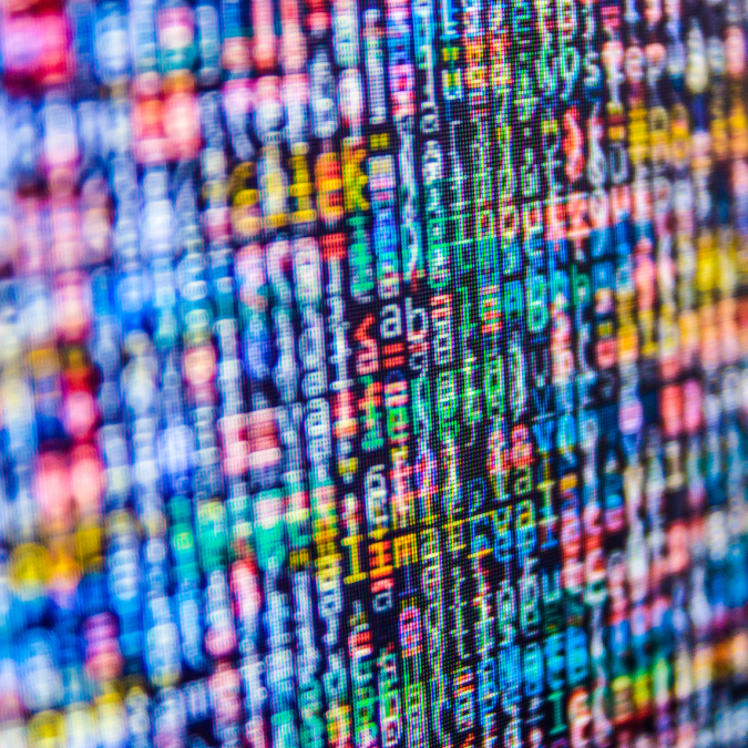 A close-up of a computer screen displaying colorful, blurred lines of code in various programming languages, with characters and symbols in shades of blue, red, green, and yellow.