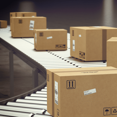 Cardboard boxes with shipping labels move along a conveyor belt in a warehouse or distribution center, illustrating a package sorting or shipping process.