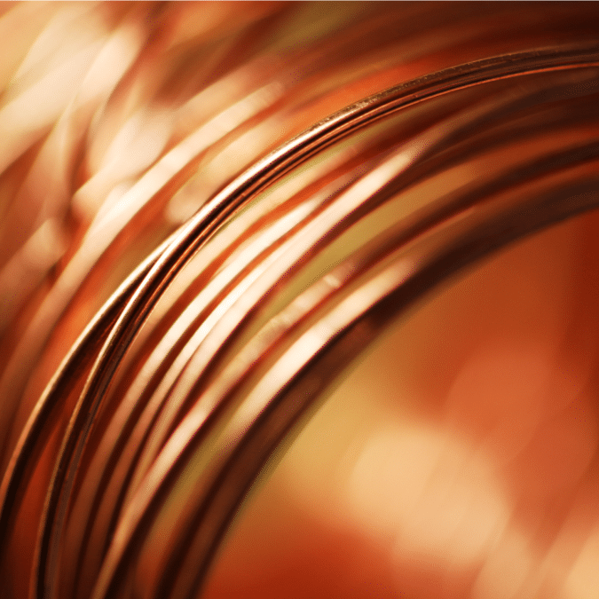 Close-up of several copper wires elegantly coiled together, with a warm, out-of-focus copper-toned background that emphasizes the metallic sheen and curved lines of the wires.