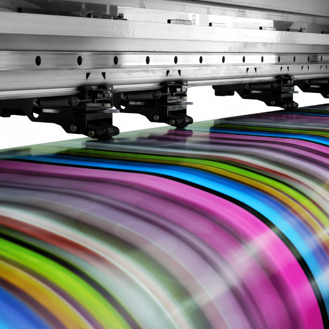 A large industrial printer prints a vibrant, multicolored pattern with stripes of pink, green, blue, yellow, and black on glossy material.