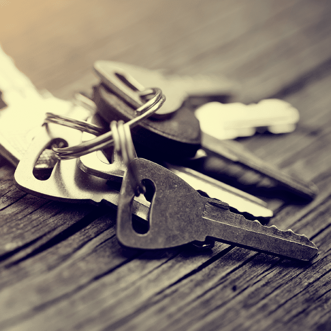 A close-up image of a set of metal keys on a keyring resting on a wooden surface, with a soft, warm light shining from the left side.