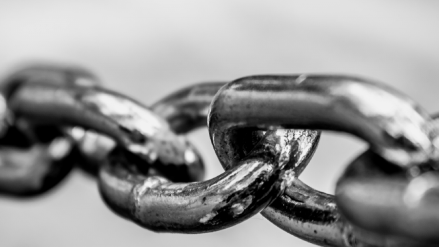 Close-up, black and white photo of metal chain links, with one link in sharp focus and the others fading into a blurred background.