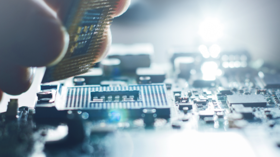 A close-up of a hand installing a computer processor onto a motherboard, with a soft light illuminating the circuit board and electronic components.