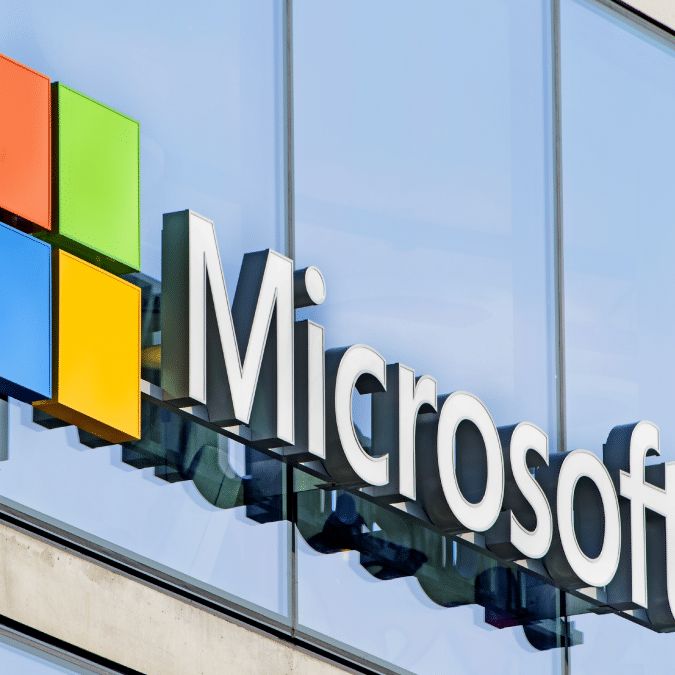 The Microsoft logo featuring a colorful window symbol and the word Microsoft in large letters is displayed on the exterior of a modern glass building.