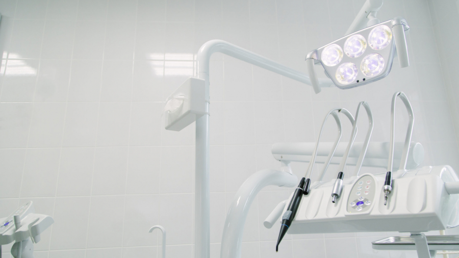 A close-up of modern dental equipment in a brightly lit, clean dental clinic, featuring overhead lights and various dental tools against a white tiled wall.