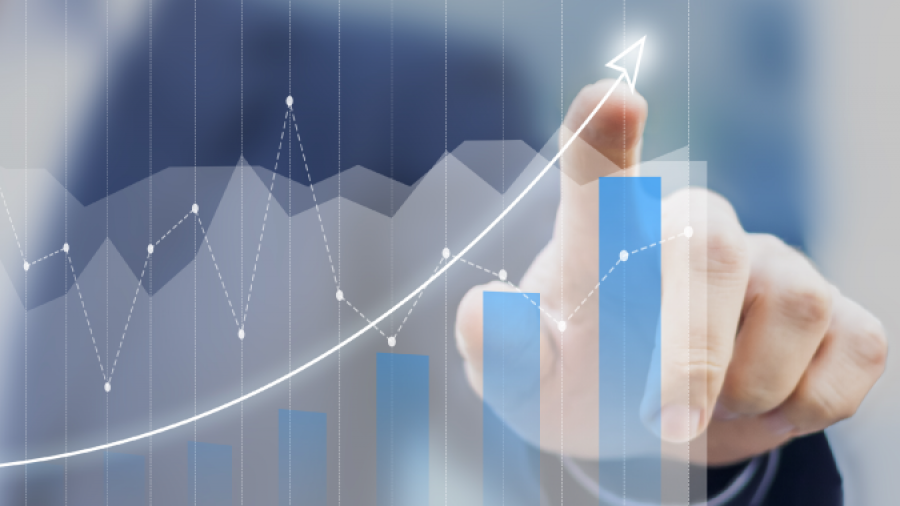 A person in a suit points to a rising bar and line graph on a transparent screen, symbolizing business growth and upward trends.