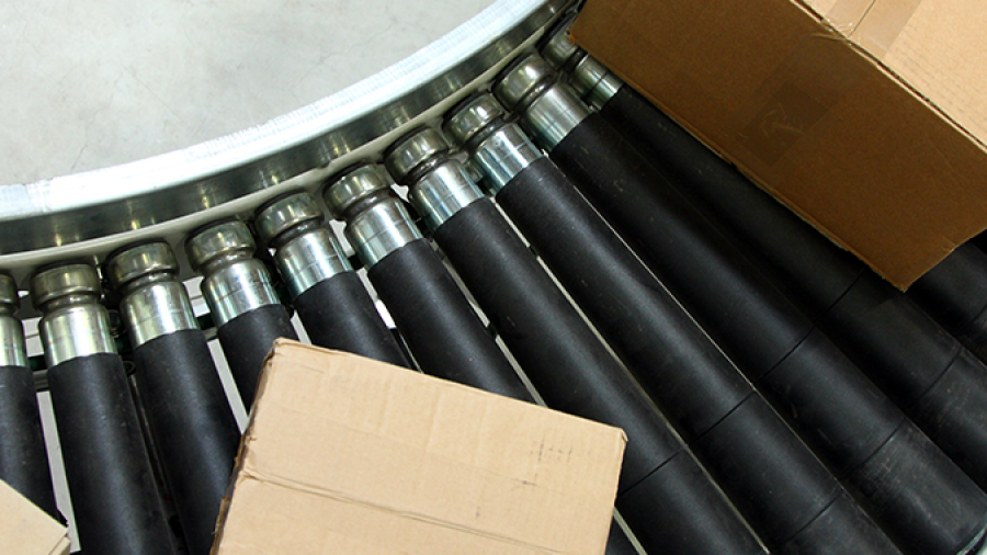 Three cardboard boxes on a curved, black roller conveyor belt, used for moving packages in a warehouse or shipping facility. The surface underneath is a smooth light gray.