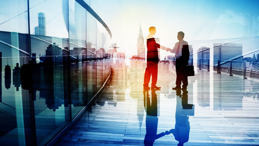 Two businesspeople shake hands on a modern rooftop or terrace with city skyscrapers in the background, sunlight streaming through, and their reflections visible on the shiny floor.
