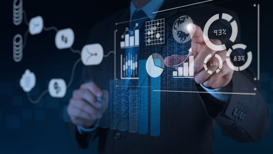 A person in a business suit interacts with virtual data visualizations, including charts, graphs, and circular progress indicators, projecting from a transparent screen in a dark, tech-themed environment.