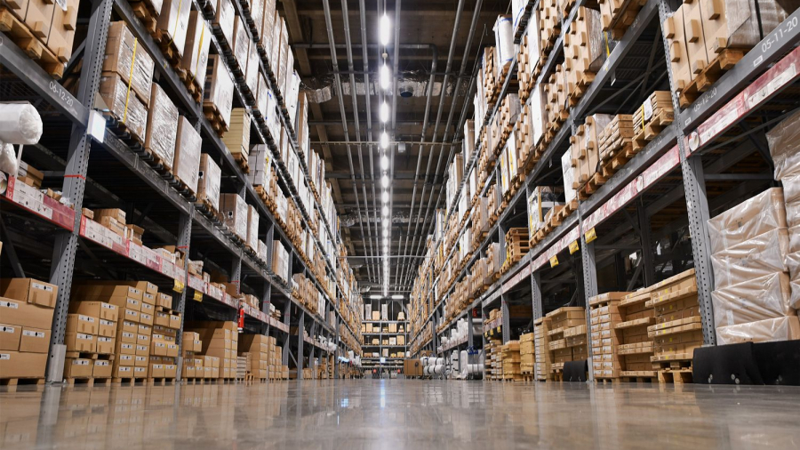 Wide-angle view of a warehouse aisle with tall shelves stacked with various cardboard boxes, illuminated by bright overhead lights and a shiny concrete floor—ideal for conducting a thorough warehouse capacity analysis.
