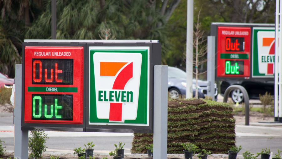 A 7-Eleven gas station sign displays Out for both regular unleaded and diesel fuels, indicating they are unavailable. Another similar sign is visible in the background. Small plants surround the signs.