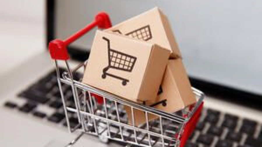 A small shopping cart filled with cardboard boxes, each featuring a shopping cart icon, sits on a laptop keyboard, representing online shopping or e-commerce.