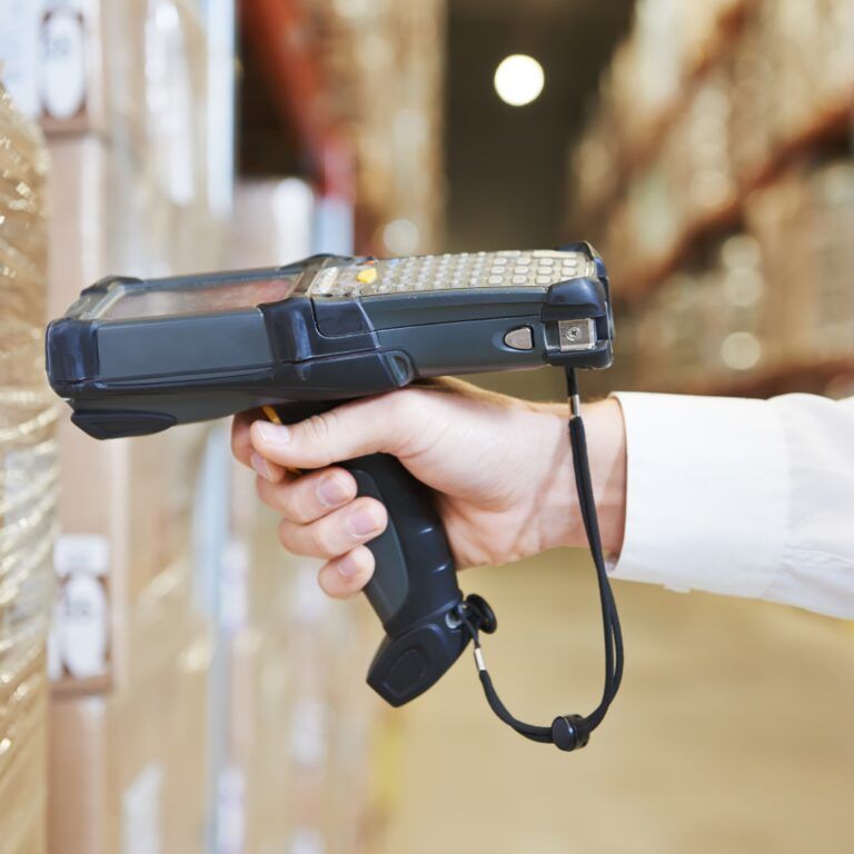 A person scans a barcode on a pallet wrapped in plastic using a handheld barcode scanner in a warehouse setting, ensuring food traceability throughout the supply chain.