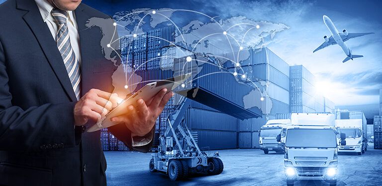 A man in a suit uses a tablet in front of shipping containers, trucks, and a plane, with a digital world map and network lines representing global logistics and transportation.