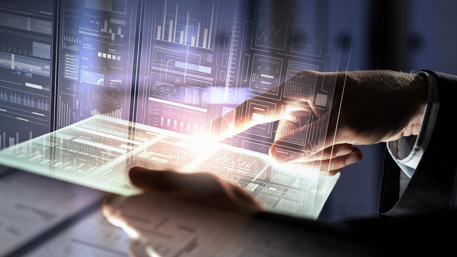 A person’s hand interacts with a glowing, transparent tablet displaying digital graphs and charts, with futuristic data visualizations projected in the background.