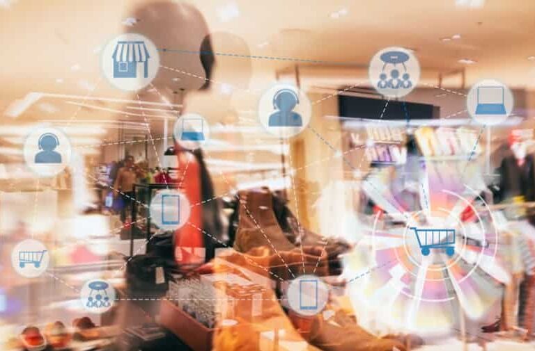 Clothing store interior with blurred mannequins and racks, overlaid with digital icons representing online shopping, carts, stores, and networking, illustrating omnichannel retail or e-commerce concepts.