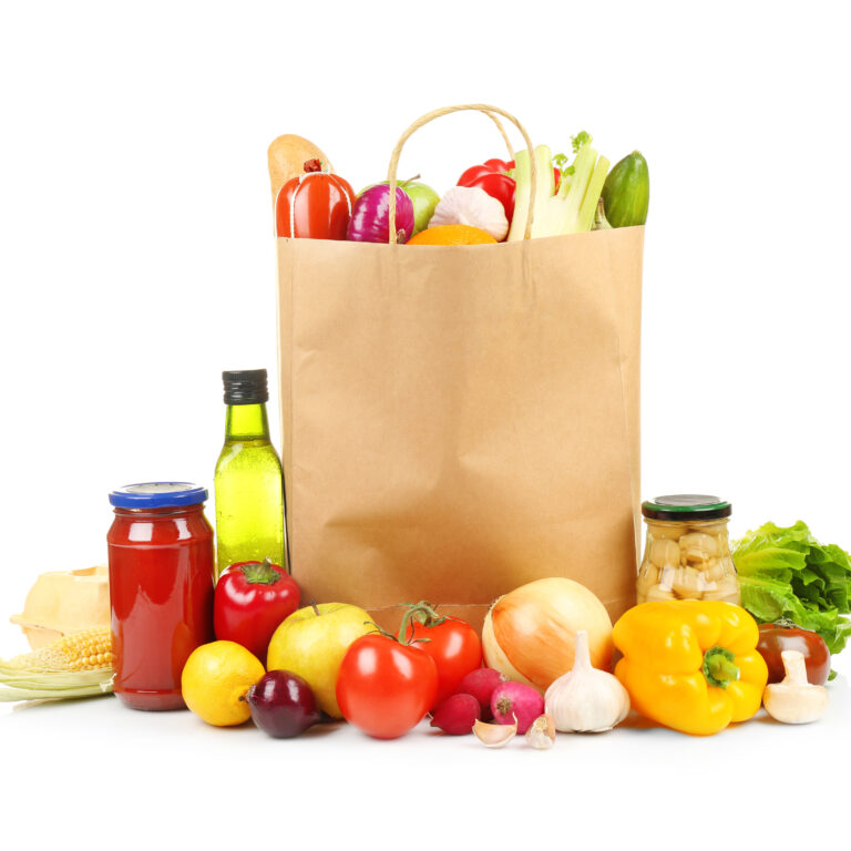 A paper grocery bag filled with fresh vegetables, surrounded by tomatoes, bell peppers, garlic, and more—perfectly arranged to highlight smart distribution consulting for quality produce on a white background.