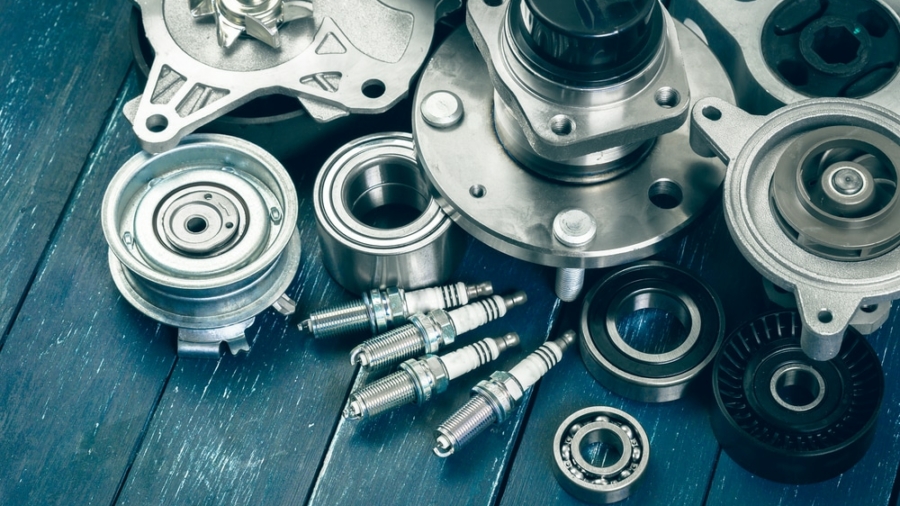 Assorted car engine parts, including spark plugs, bearings, pulleys, and metal components, arranged on a blue wooden surface.