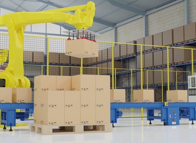 A yellow robotic arm performs automated palletization, moving cardboard boxes onto a conveyor belt in a warehouse filled with shelves of boxes and industrial equipment.
