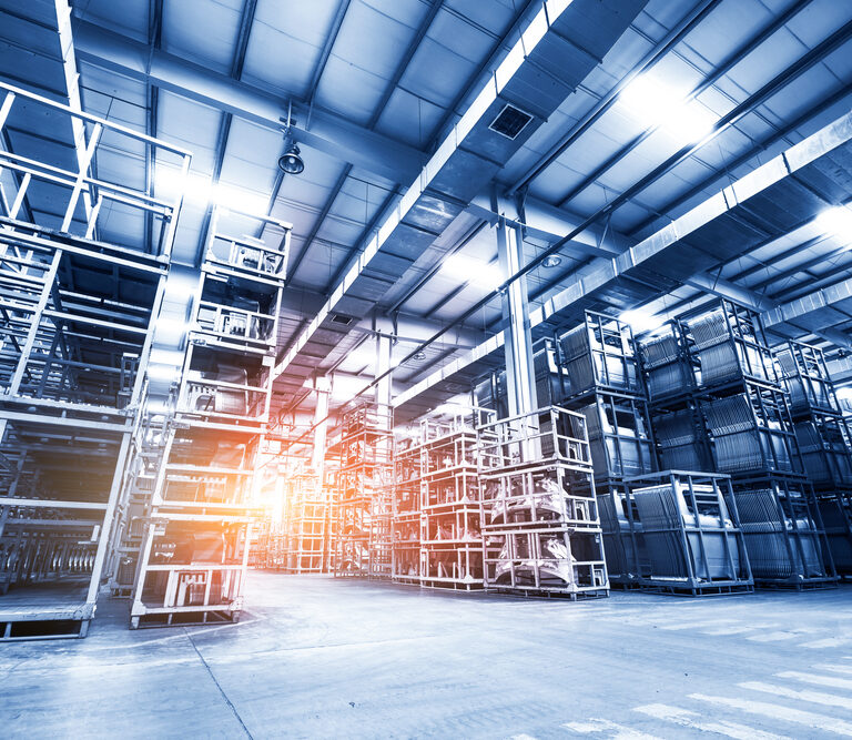 Large, modern warehouse interior with tall metal storage racks and wide aisles, optimized for slam line automation. Bright lighting and a warm sun flare fill the facility, creating a clean, organized atmosphere.