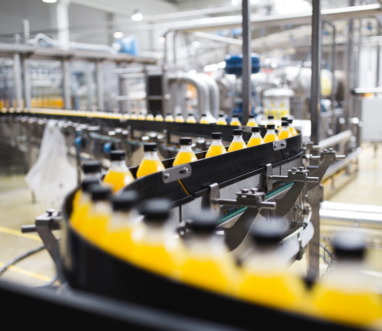 A bottling plant production line showcases automation strategies, with rows of yellow-capped bottles filled with orange liquid moving along conveyor belts in an industrial setting.