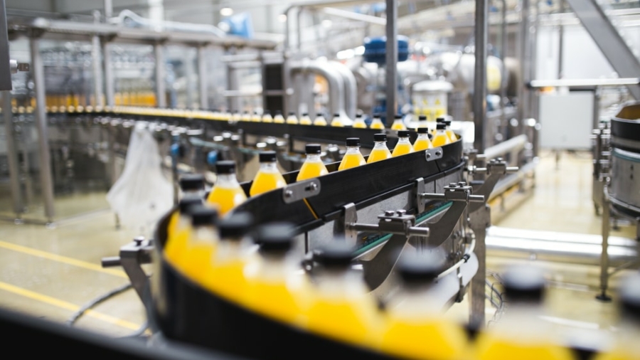 A bottling plant production line showcases automation strategies, with rows of yellow-capped bottles filled with orange liquid moving along conveyor belts in an industrial setting.