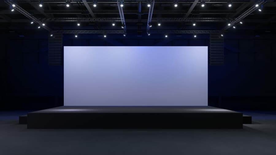 A large, empty stage with a wide, blank screen is lit by overhead spotlights in a dark, spacious auditorium—perfect for unveiling insights from a WMS Implementation Case Study.