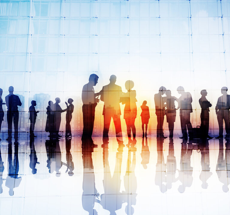 Silhouettes of business people discussing S&OP strategies in groups by large glass windows, their reflections on the shiny floor and a cityscape visible through the glass.