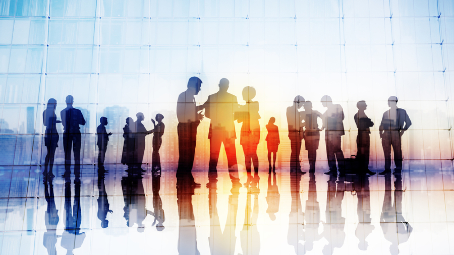 Silhouettes of business people discussing S&OP strategies in groups by large glass windows, their reflections on the shiny floor and a cityscape visible through the glass.