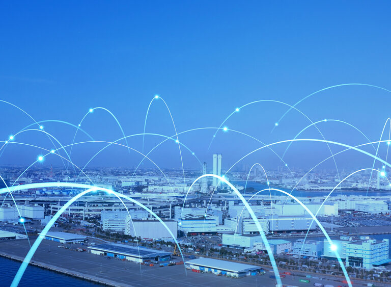 A cityscape by the water with white and blue glowing arcs illustrating a network or data connections, symbolizing connectivity and modern technology in urban infrastructure.