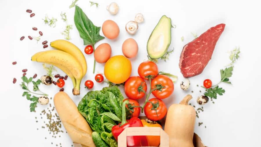 A paper bag overflows with fresh groceries, including tomatoes, lettuce, and more—all carefully selected to highlight supply chain traceability—arranged on a white background.