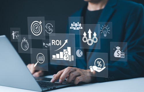 A person in a suit types on a laptop with floating digital icons, including graphs, a target, gears, and symbols representing ROI and financial growth—conveying the efficiency of a Transportation Management System.