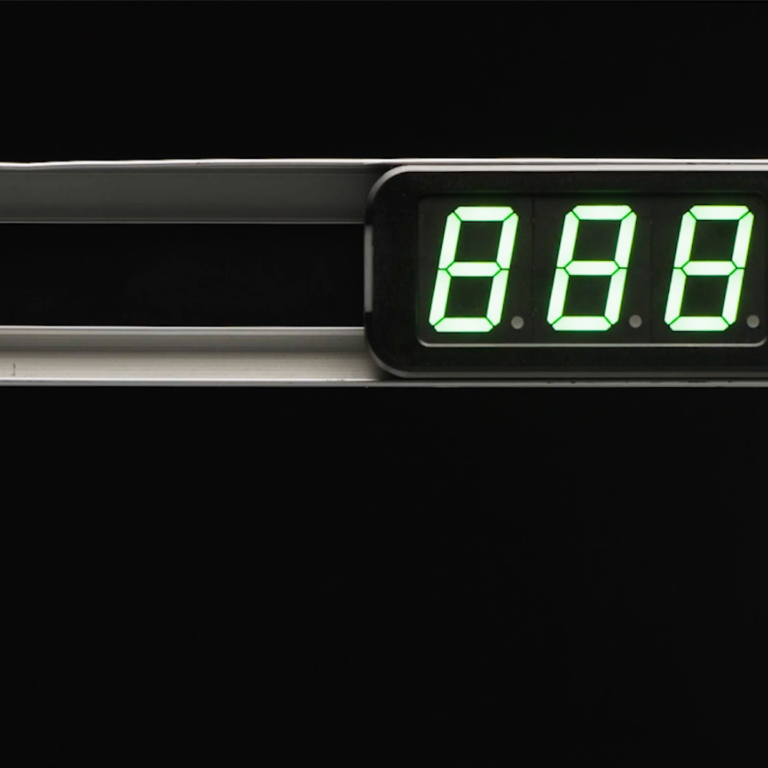 A digital display with bright green numbers reading 888 is mounted on a metallic surface against a black background, suggesting its use in a warehouse setting. The device also features a small circular button and the enMotion logo.