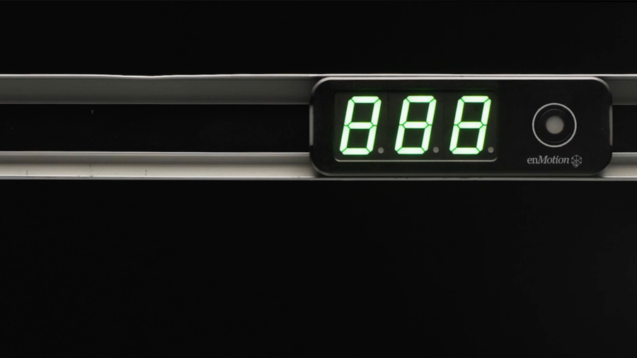 A digital display with bright green numbers reading 888 is mounted on a metallic surface against a black background, suggesting its use in a warehouse setting. The device also features a small circular button and the enMotion logo.