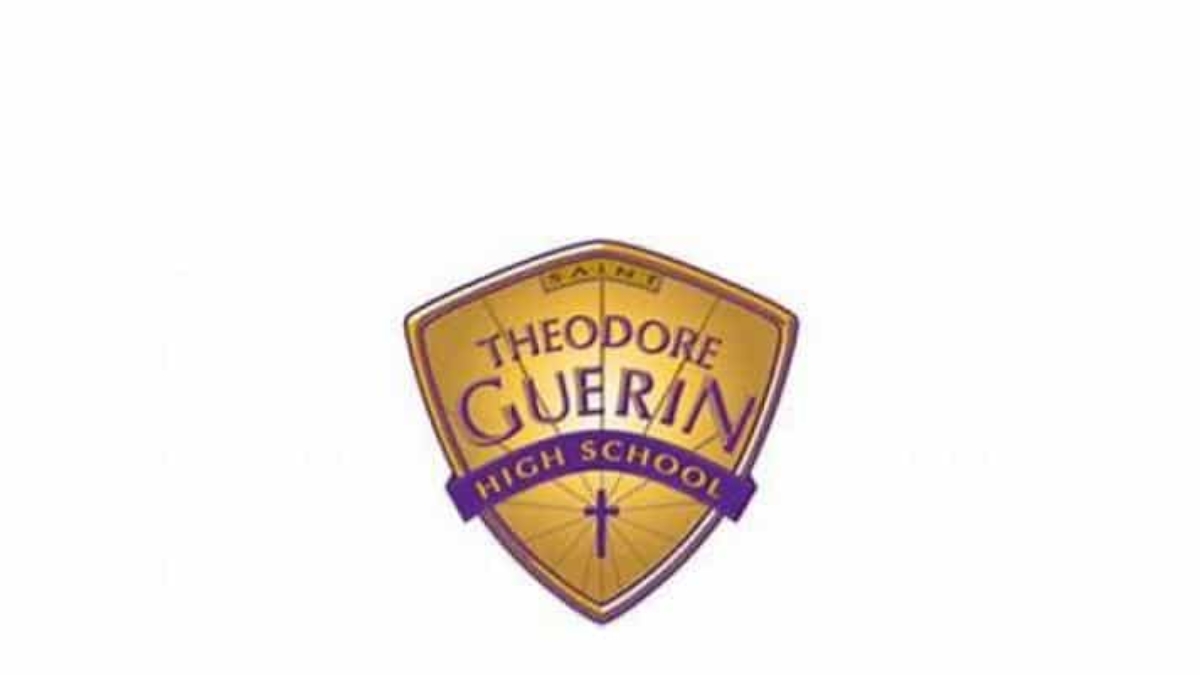 Shield-shaped gold and purple logo for Theodore Guerin High School, featuring the school name and a small cross near the bottom.