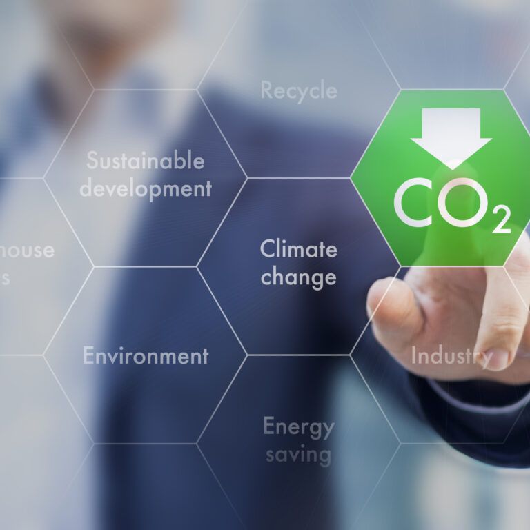 A person presses a digital hexagon labeled CO₂ with a downward arrow on a transparent screen. Surrounding hexagons display words like Climate change, Sustainable development, and Environment.