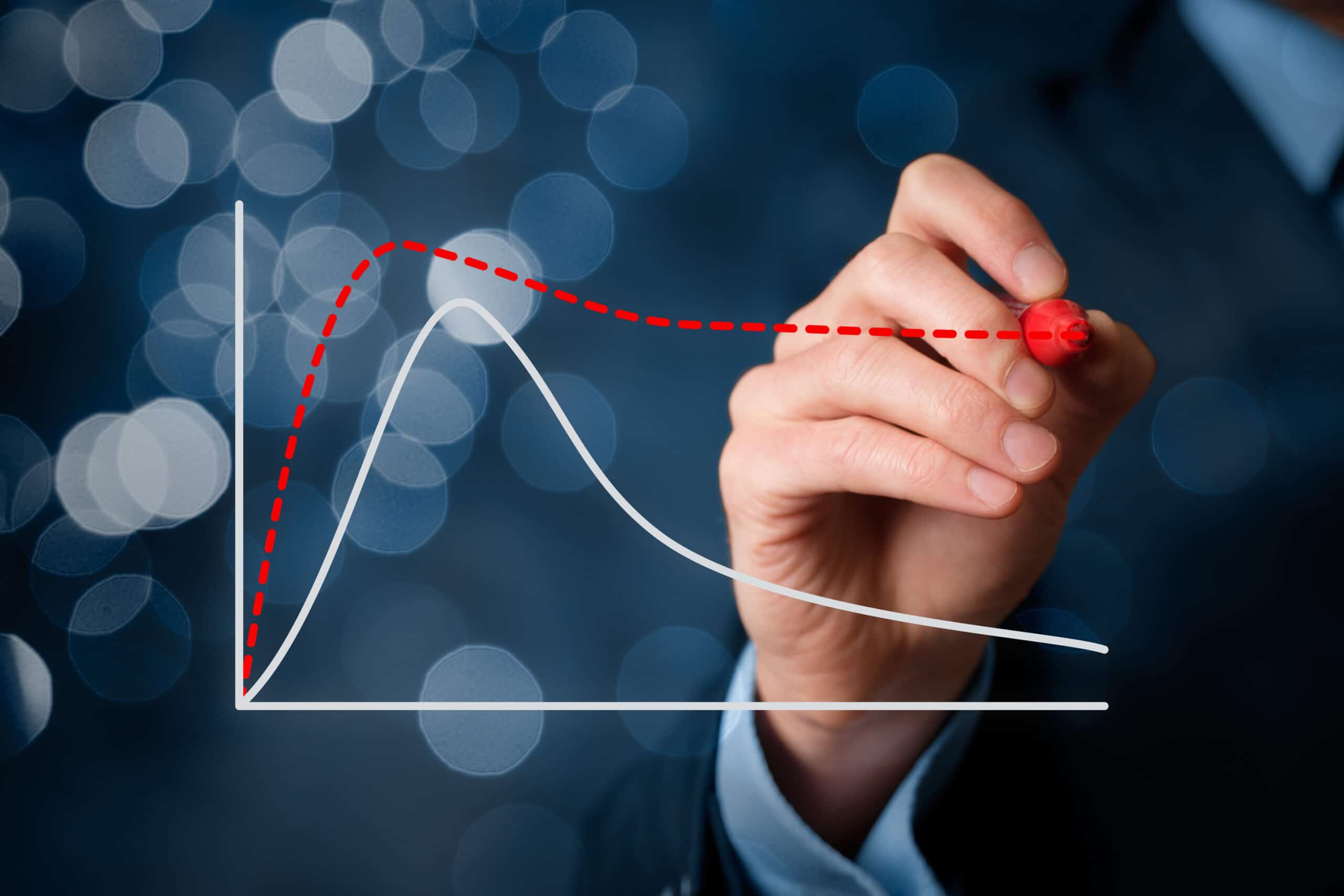 A hand in a suit draws a red dashed trend line above a white line graph on a transparent screen, with blurred blue lights in the background.