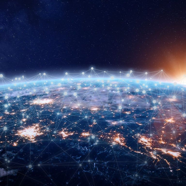 A view of Earth from space at sunrise, with illuminated city lights and a digital network of interconnected glowing points and lines superimposed over the surface, symbolizing global connectivity.
