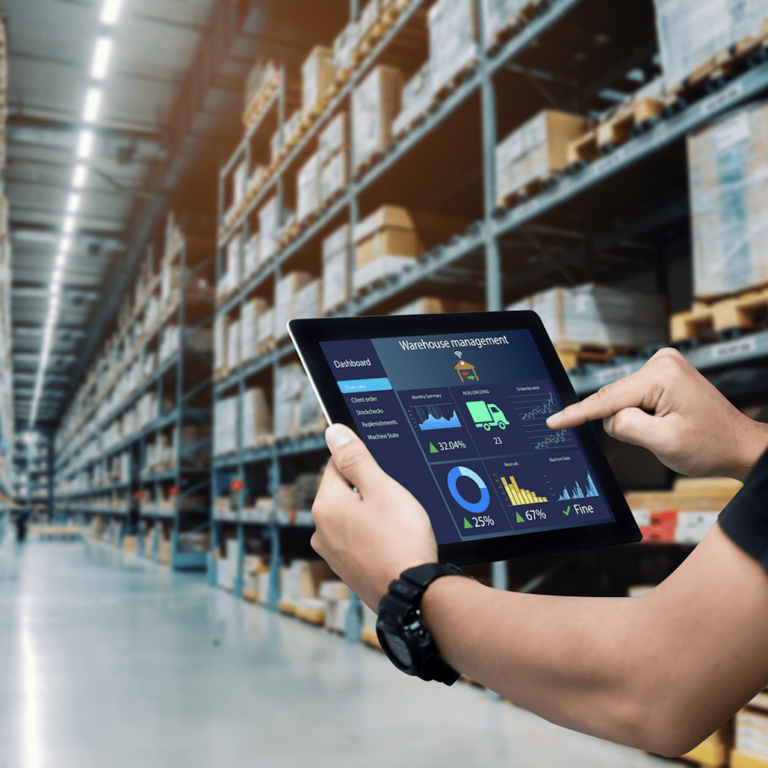 A person uses a tablet displaying warehouse management software in a large warehouse filled with shelves and boxes, highlighting digital inventory control and the benefits of warehouse automation technologies.