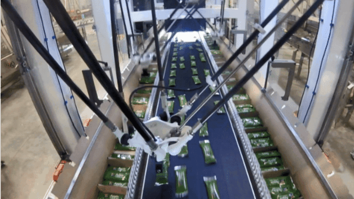 Overhead view of an automated robotic arm sorting green rectangular packages on a conveyor belt inside a large industrial facility.