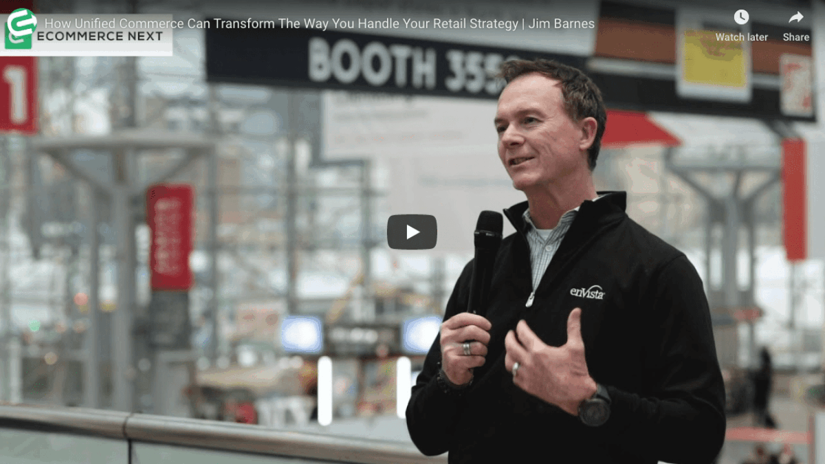 A man in a black jacket speaks into a microphone at an indoor event, with blurred signs and people in the background. The video title is How Unified Commerce Can Transform The Way You Handle Your Retail Strategy | Jim Barnes.