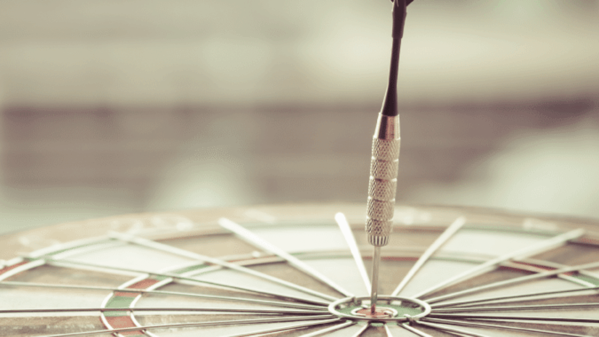 A dart is precisely embedded in the bullseye of a dartboard, illustrating accuracy and focus; the background is softly blurred, keeping the attention on the dart and the target.