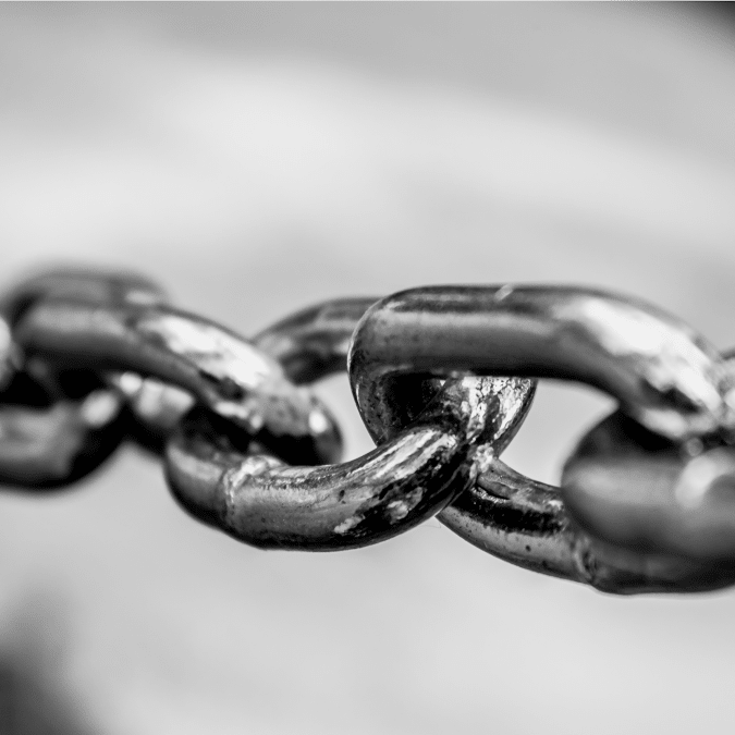 Close-up black and white photo of a metal chain, focusing on several interlinked, shiny chain links with a blurred background.